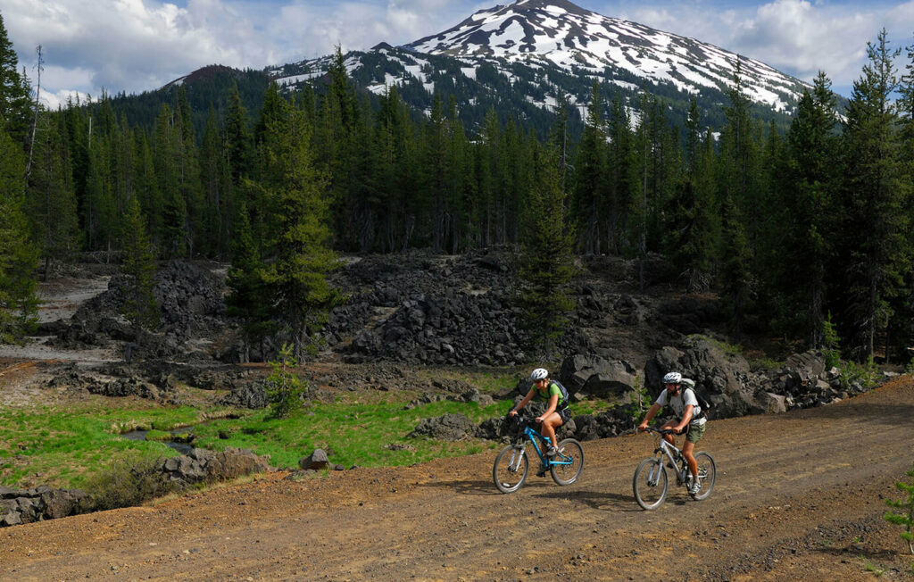 Couple mountain biking with Mount Bachelor behind in them