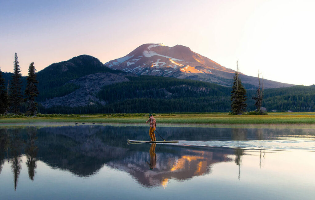 Person paddle boarding on a lake with Mount Bachelor behind in the distance