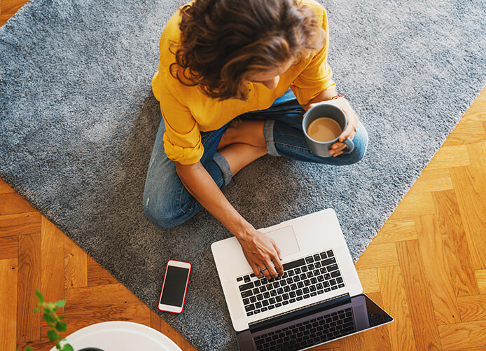 Woman sitting on the floor with a cup of coffee looking at her laptop computer